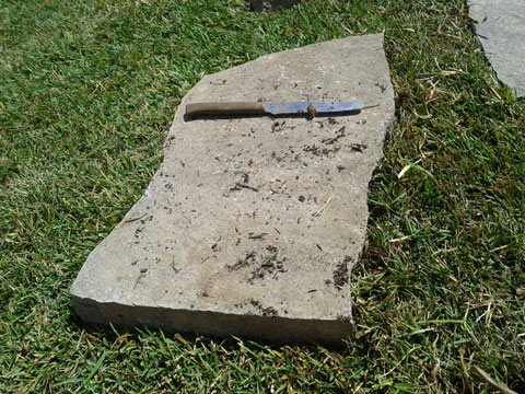Inizio del posizionamento di una mattonella di porfido nel proprio giardino con prato pronto.